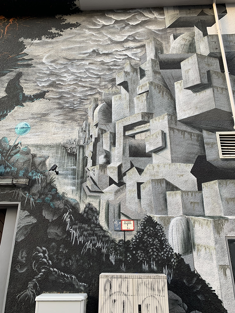abstraktes Mural in Grautönen, es sind Wolken, Pflanzen und Steinböcke dargestellt, einziger Farbtupfer ein Kreis / Lollie, Ballon in Türkis